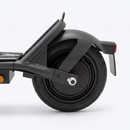 Close-up rear view of a black electric scooter or moped showing the rear wheel, black fender, frame, and a small red taillight on a clean white studio background.
