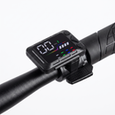 A black electronic speed display mounted on a black bicycle handlebar, showing a digital speed readout with colorful interface graphics.